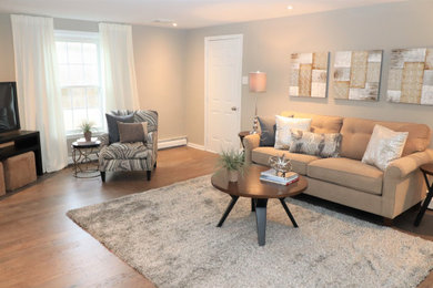 Imagen de sala de estar abierta grande sin chimenea con paredes grises, suelo de madera en tonos medios y televisor independiente