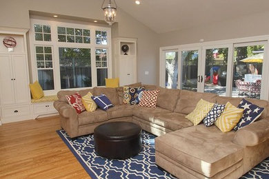 Modelo de sala de estar abierta tradicional grande con paredes beige, suelo de madera clara, suelo marrón y televisor colgado en la pared