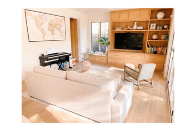 Diseño de sala de estar con biblioteca abierta campestre de tamaño medio con paredes blancas, suelo de madera clara y pared multimedia