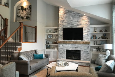 Источник вдохновения для домашнего уюта: большая открытая гостиная комната в современном стиле с серыми стенами, паркетным полом среднего тона, стандартным камином, фасадом камина из камня, телевизором на стене и оранжевым полом