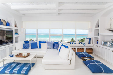 На фото: гостиная комната в морском стиле с белыми стенами, деревянным полом, мультимедийным центром и белым полом с