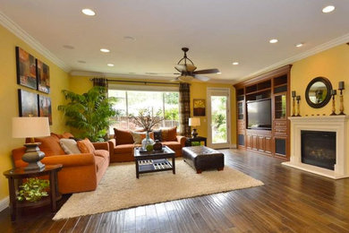 Diseño de sala de estar cerrada tropical grande con paredes amarillas, suelo de madera en tonos medios, todas las chimeneas, marco de chimenea de piedra, pared multimedia y suelo marrón