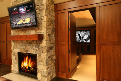 Photo of a medium sized traditional open plan games room in Chicago with brown walls, medium hardwood flooring, a standard fireplace, a stone fireplace surround, a wall mounted tv and brown floors.
