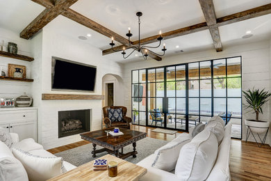Foto de sala de estar tradicional renovada con paredes blancas, suelo de madera en tonos medios, todas las chimeneas, marco de chimenea de ladrillo, televisor colgado en la pared, suelo marrón y alfombra