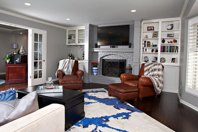 Modelo de sala de estar abierta tradicional renovada de tamaño medio con paredes grises, suelo de madera oscura, todas las chimeneas, marco de chimenea de ladrillo y televisor colgado en la pared