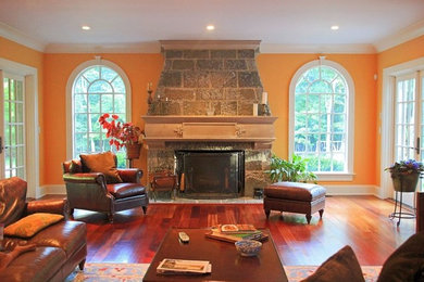 Large elegant enclosed medium tone wood floor family room photo in New York with orange walls, a standard fireplace, a stone fireplace and no tv