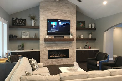 Example of a mid-sized transitional open concept dark wood floor and brown floor family room design in Other with a wall-mounted tv, gray walls, a standard fireplace and a stone fireplace