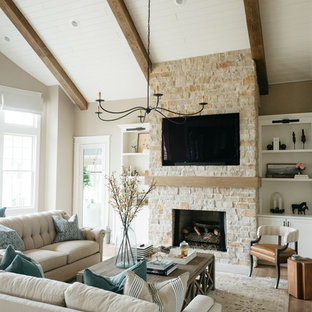 Cette image montre une grand salle de séjour rustique fermée avec un mur beige, un sol en bois clair, une cheminée standard, un manteau de cheminée en pierre, un téléviseur encastré et un sol marron.