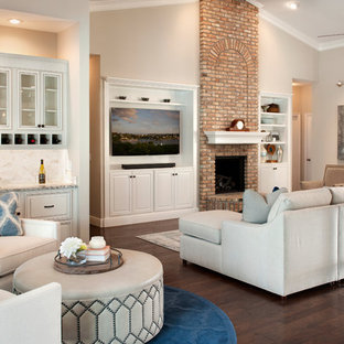 Foto de sala de estar con barra de bar abierta, mediterránea, con paredes beige, suelo de madera oscura, chimenea tradicional, marco de chimenea de ladrillo, pared multimedia y suelo marrón