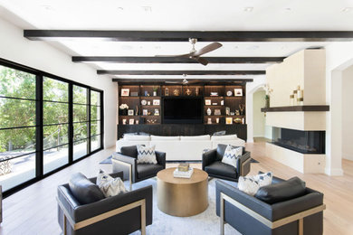 Foto de sala de estar abierta tradicional renovada grande con paredes blancas, suelo de madera clara, chimenea lineal, marco de chimenea de piedra, pared multimedia y vigas vistas