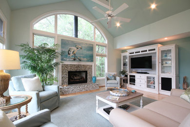 Modelo de sala de estar abierta marinera grande con paredes azules, suelo de madera clara, todas las chimeneas, marco de chimenea de baldosas y/o azulejos y televisor independiente