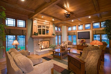Imagen de sala de estar abierta de estilo americano grande con paredes verdes, suelo de madera en tonos medios, todas las chimeneas, marco de chimenea de piedra y televisor colgado en la pared