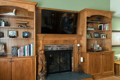 Modelo de sala de estar abierta tradicional renovada con paredes verdes, suelo de madera clara, todas las chimeneas, marco de chimenea de ladrillo y televisor colgado en la pared