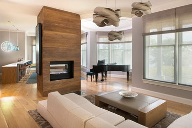 Ejemplo de sala de estar abierta moderna grande con chimenea de doble cara, marco de chimenea de madera y televisor retractable