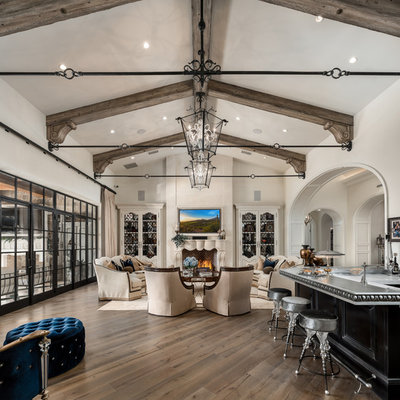 Example of a huge tuscan open concept medium tone wood floor and brown floor family room design in Phoenix with a bar, white walls, a standard fireplace, a stone fireplace and a wall-mounted tv