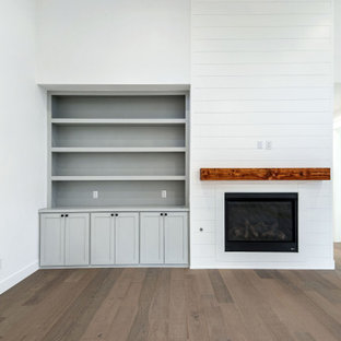Esempio di un soggiorno country di medie dimensioni e aperto con pareti bianche, parquet chiaro, camino classico, cornice del camino in perlinato, TV a parete, pavimento beige, travi a vista e pareti in perlinato