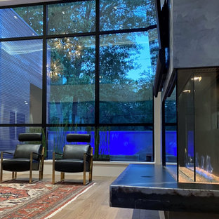 Geräumiges, Offenes Modernes Wohnzimmer mit weißer Wandfarbe, hellem Holzboden, Tunnelkamin, Kaminumrandung aus Metall, Wand-TV und eingelassener Decke in Houston