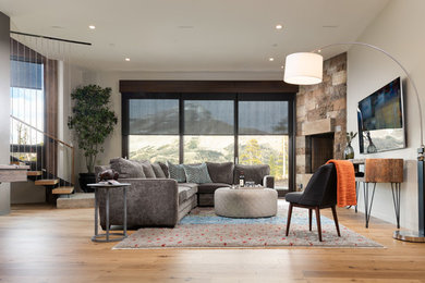 Modelo de sala de estar rural con paredes beige, suelo de madera en tonos medios, chimenea de esquina, marco de chimenea de piedra y suelo marrón