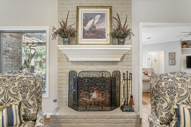 Example of a classic medium tone wood floor and brown floor family room design in Houston with beige walls, a standard fireplace and a brick fireplace