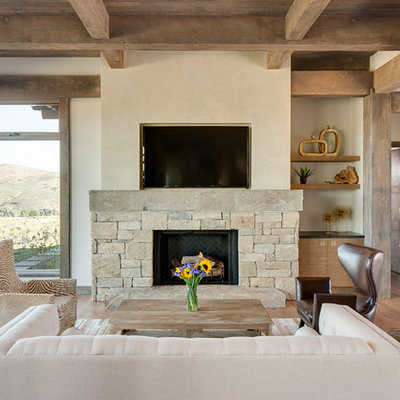 Example of a mountain style medium tone wood floor family room design in Salt Lake City with beige walls, a standard fireplace, a stone fireplace and a wall-mounted tv