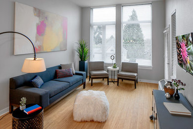 Modelo de sala de estar abierta minimalista de tamaño medio con paredes grises, suelo laminado, televisor colgado en la pared y suelo beige