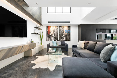 Imagen de sala de estar abierta actual de tamaño medio con suelo de cemento, televisor colgado en la pared, paredes blancas y suelo gris