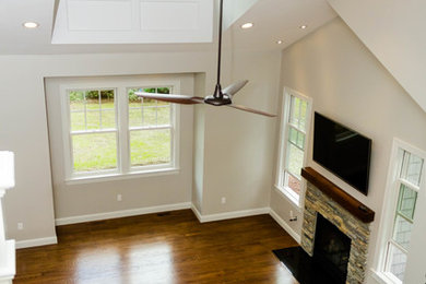 Offenes Uriges Wohnzimmer mit weißer Wandfarbe, braunem Holzboden, Kamin, Kaminumrandung aus Stein und TV-Wand in Bridgeport