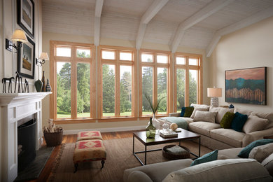 Modelo de sala de estar abierta actual con paredes beige, suelo de madera en tonos medios, todas las chimeneas y marco de chimenea de madera