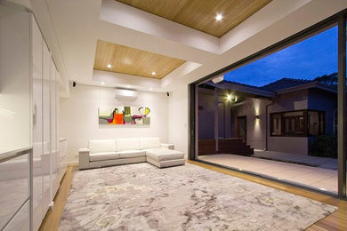 Diseño de sala de estar con barra de bar abierta actual de tamaño medio con paredes blancas, suelo de madera clara y televisor independiente