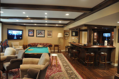Modelo de sala de estar con barra de bar abierta tradicional grande sin chimenea con paredes beige, suelo de madera en tonos medios, televisor colgado en la pared y suelo marrón