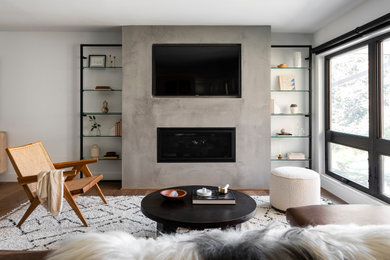 Ejemplo de sala de estar abierta actual de tamaño medio con paredes grises, suelo de madera en tonos medios, todas las chimeneas, marco de chimenea de yeso, pared multimedia y suelo marrón