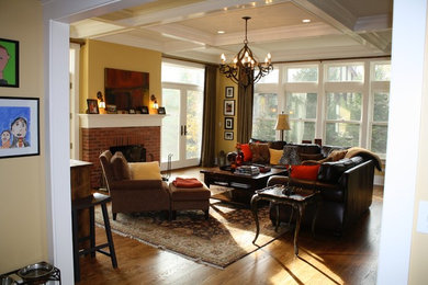 Modelo de sala de estar cerrada tradicional renovada de tamaño medio con paredes amarillas, suelo de madera oscura, todas las chimeneas, marco de chimenea de ladrillo y televisor colgado en la pared