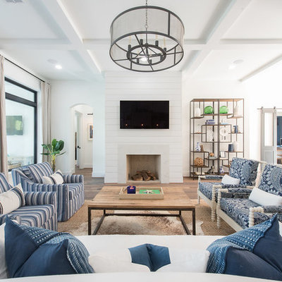 Example of a large beach style open concept brown floor and dark wood floor family room design in Houston with white walls, a standard fireplace and a wall-mounted tv