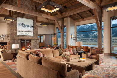 Modelo de sala de estar con barra de bar abierta de estilo americano extra grande con paredes beige, suelo de madera clara, todas las chimeneas y marco de chimenea de piedra