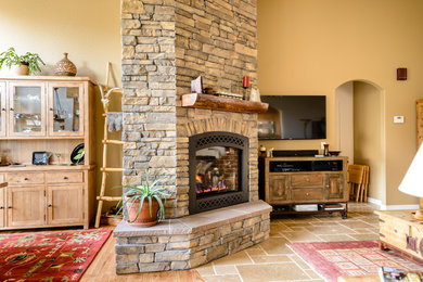 Inspiration for a large rustic open concept limestone floor and beige floor family room remodel in Denver with beige walls, a standard fireplace, a stone fireplace and a wall-mounted tv