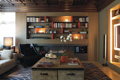 Foto de sala de estar con biblioteca abierta bohemia de tamaño medio con paredes marrones, suelo de madera en tonos medios, chimenea lineal, marco de chimenea de metal y pared multimedia