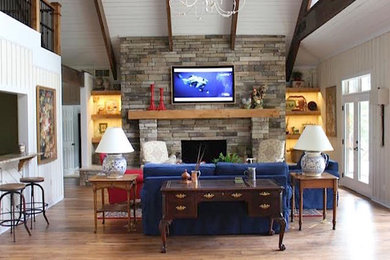 Modelo de sala de estar de estilo americano con paredes blancas, suelo de madera clara, todas las chimeneas, marco de chimenea de piedra y televisor colgado en la pared