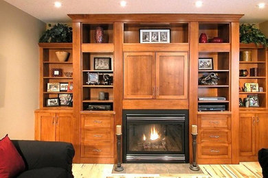 Family room library - mid-sized traditional enclosed light wood floor family room library idea in Calgary with beige walls, a standard fireplace, a wood fireplace surround and a concealed tv