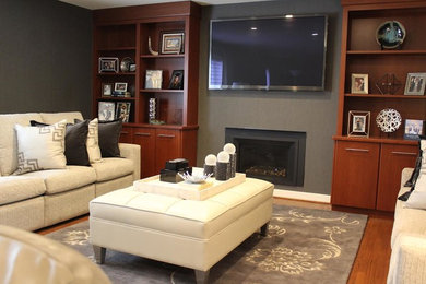 Стильный дизайн: изолированная гостиная комната среднего размера в классическом стиле с серыми стенами, паркетным полом среднего тона, стандартным камином, фасадом камина из штукатурки, телевизором на стене и коричневым полом - последний тренд