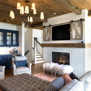 Example of a large beach style brown floor and dark wood floor family room design in Minneapolis with a bar, white walls, a two-sided fireplace, a brick fireplace and a concealed tv