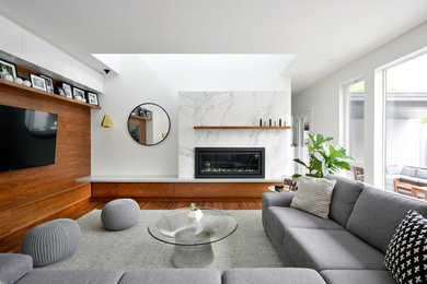 Imagen de sala de estar contemporánea con paredes blancas, suelo de madera en tonos medios, chimenea lineal, marco de chimenea de piedra y pared multimedia