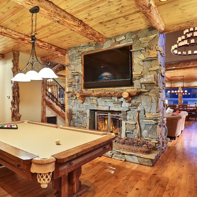 Inspiration for a mid-sized rustic open concept medium tone wood floor game room remodel in Los Angeles with beige walls, a two-sided fireplace, a stone fireplace and a wall-mounted tv