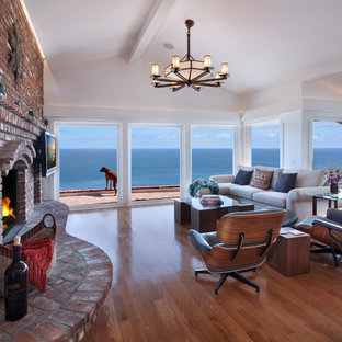 Foto de sala de estar cerrada, de estilo americano, grande, con paredes blancas, suelo de madera clara, chimenea tradicional, marco de chimenea de ladrillo, televisor colgado en la pared y suelo beige