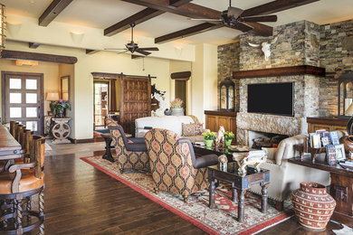 Southwest open concept dark wood floor family room photo in Phoenix with beige walls, a standard fireplace, a stone fireplace and a wall-mounted tv