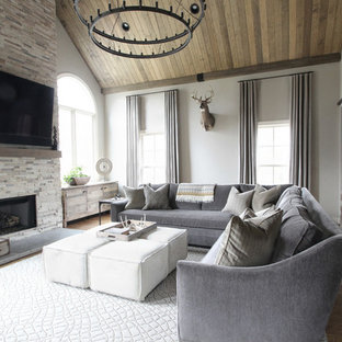 Foto de sala de estar clásica renovada, grande, con paredes beige, suelo de madera en tonos medios, chimenea tradicional, marco de chimenea de piedra y televisor colgado en la pared