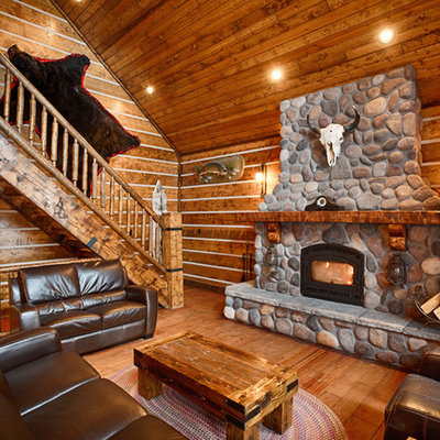 Inspiration for a large rustic enclosed dark wood floor and brown floor family room remodel in Other with brown walls, a wood stove, a stone fireplace and a wall-mounted tv