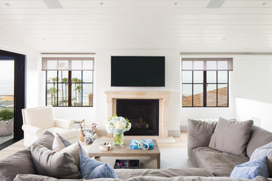 ロサンゼルスにある高級な巨大なビーチスタイルのおしゃれな独立型ファミリールーム (白い壁、淡色無垢フローリング、標準型暖炉、石材の暖炉まわり、壁掛け型テレビ、ベージュの床) の写真