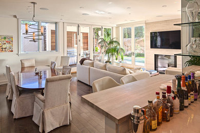 Medium sized contemporary open plan games room in Los Angeles with white walls, dark hardwood flooring, a standard fireplace, a wooden fireplace surround, a wall mounted tv and brown floors.