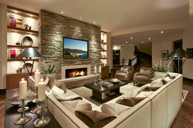 Imagen de sala de estar abierta clásica renovada grande con paredes beige, suelo de madera en tonos medios, todas las chimeneas, marco de chimenea de piedra y televisor colgado en la pared