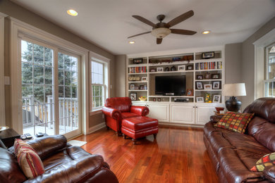 Modelo de sala de estar con biblioteca abierta tradicional de tamaño medio con paredes grises, suelo de madera en tonos medios y pared multimedia
